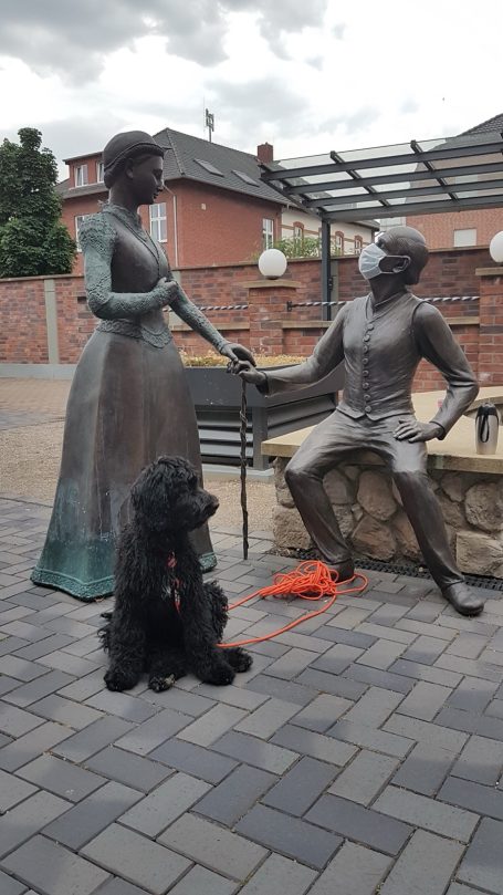 Bronzestatue eines Paares, sitzend und stehend, mit einem Bernedoodle davor.