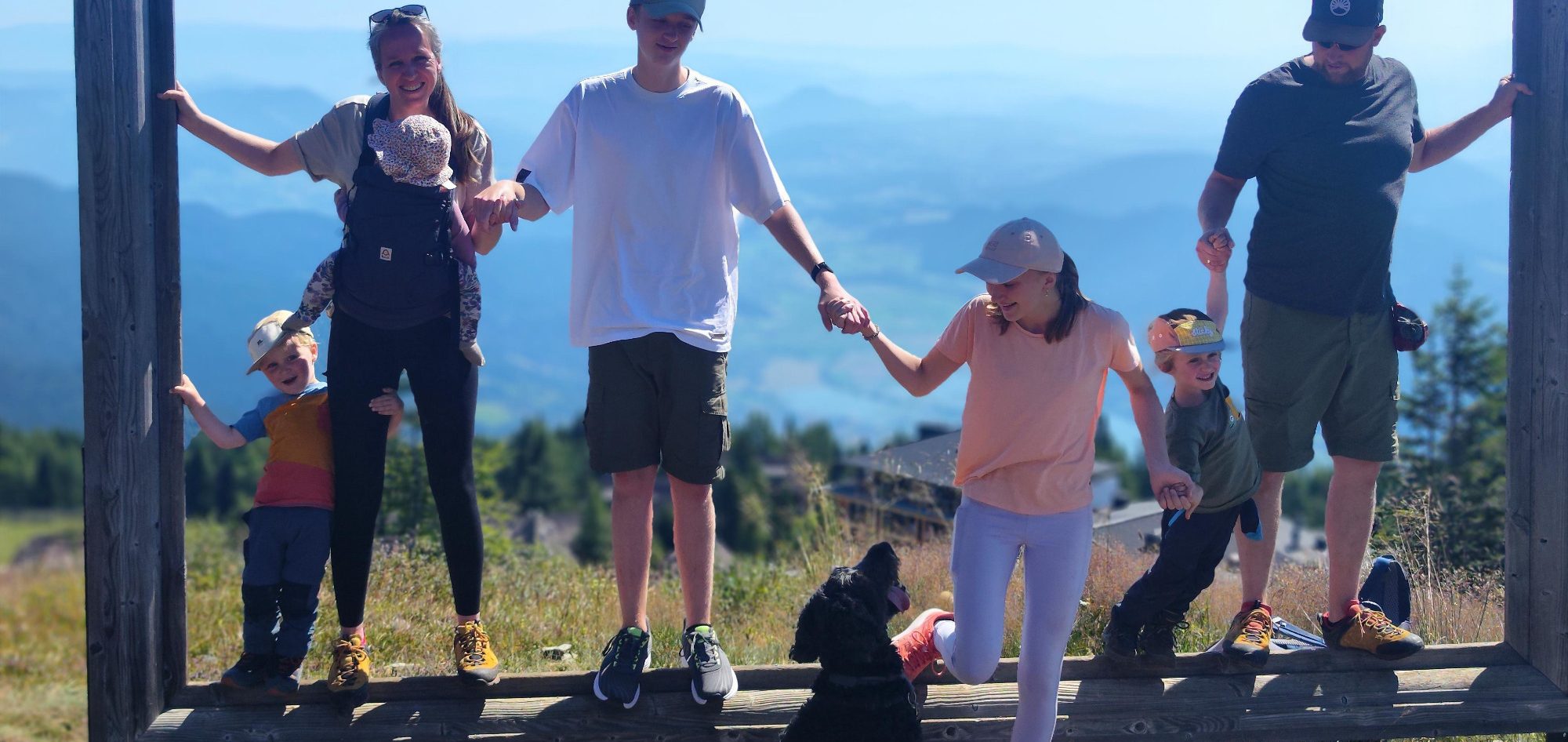 Die Familie mit Kindern und dem Bernedoodle stehen in einem großem Fotorahmen auf einem hohen Berg mit Weitblick, halten sich an den Händen.